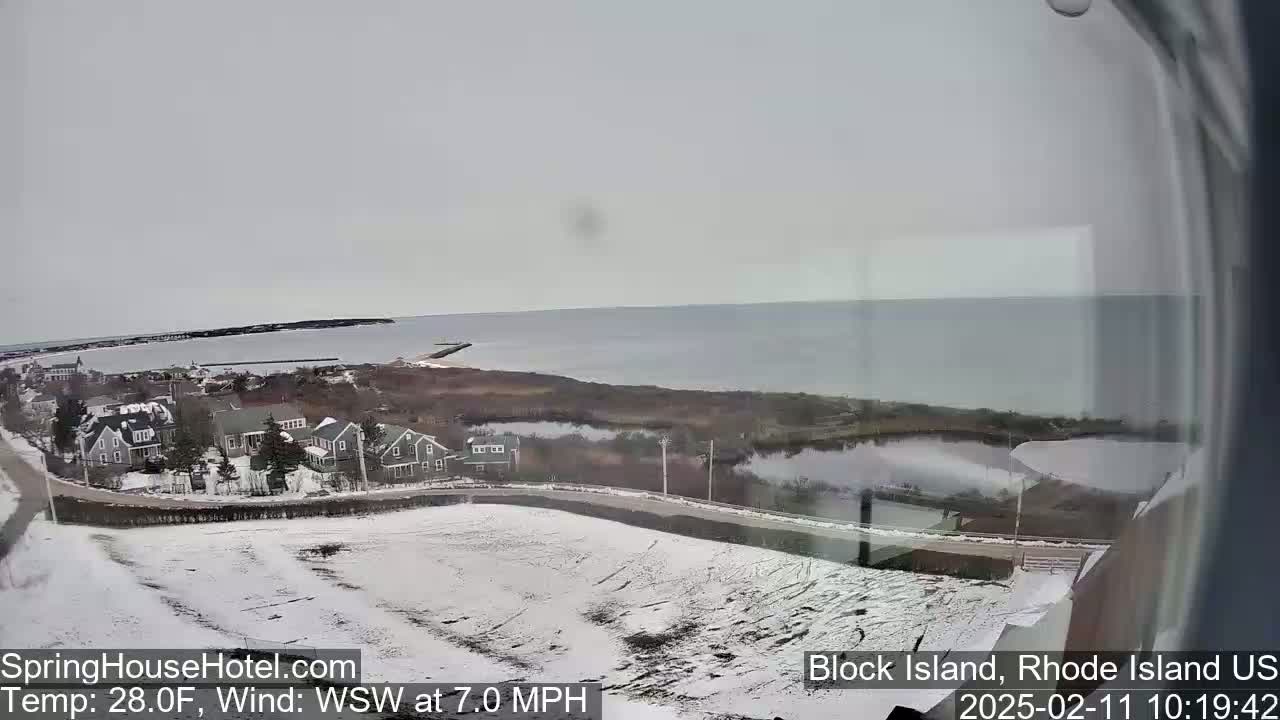 A snow-covered coastal town overlooks a calm body of water under an overcast sky.