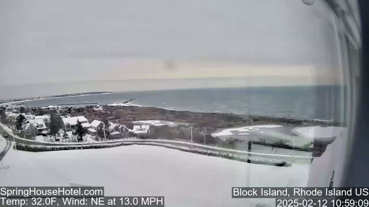 A snow-covered coastal town overlooks a choppy ocean under an overcast sky.