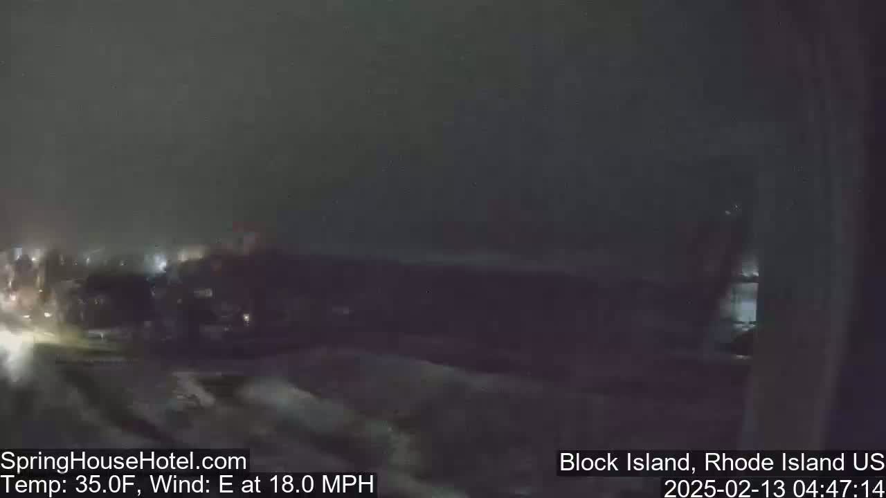 A nighttime, blurry view of a parking lot with some cars, under dark and stormy conditions with an 18 mph east wind.