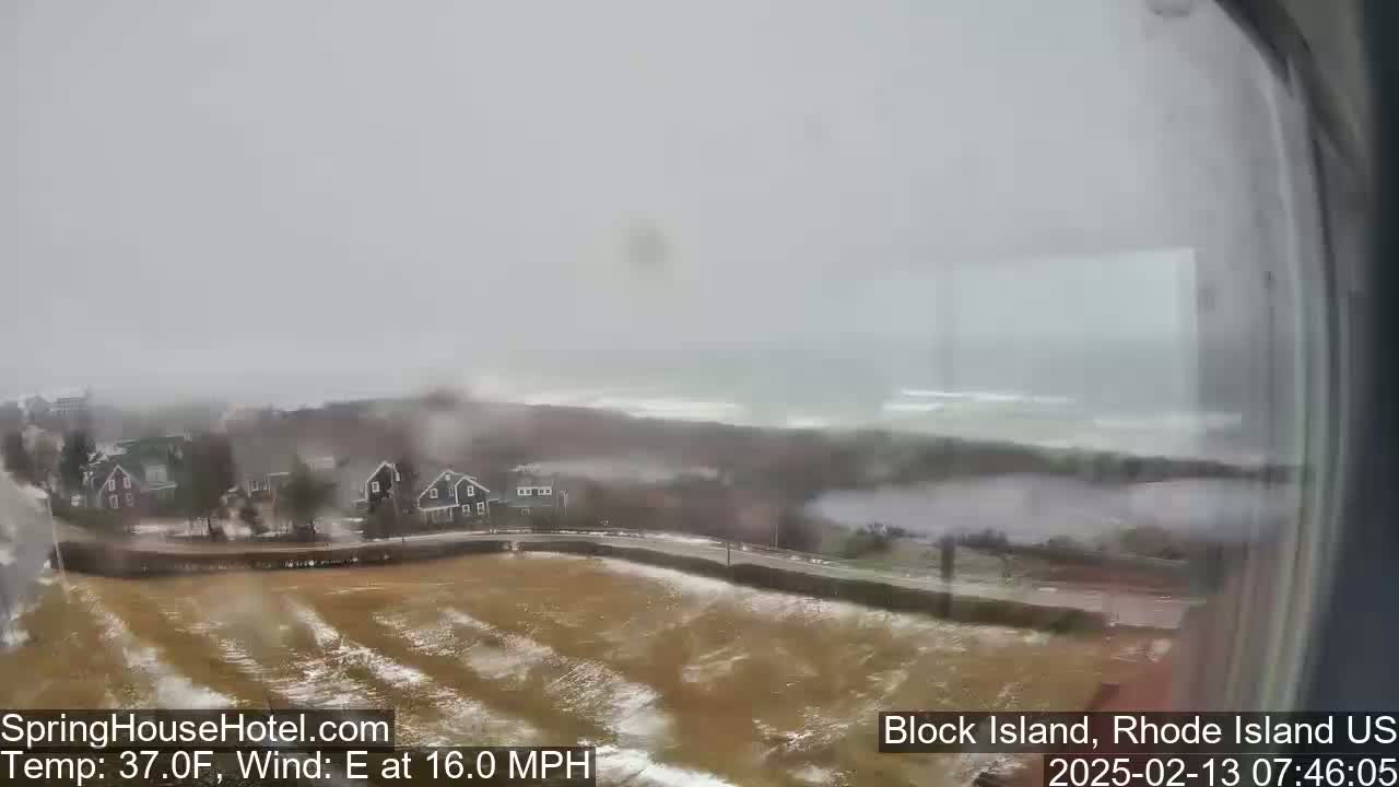 A snowy, overcast coastal scene shows houses and a road, with a windy,  eastward blowing wind and a temperature of 37 degrees Fahrenheit.