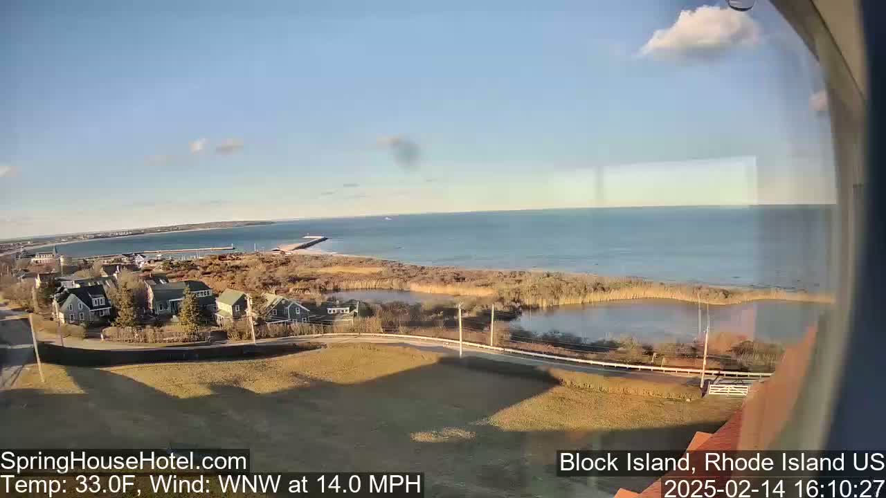 A coastal scene on a partly sunny day with a 14 mph wind shows a calm ocean, a marshy area, and several houses near the water.
