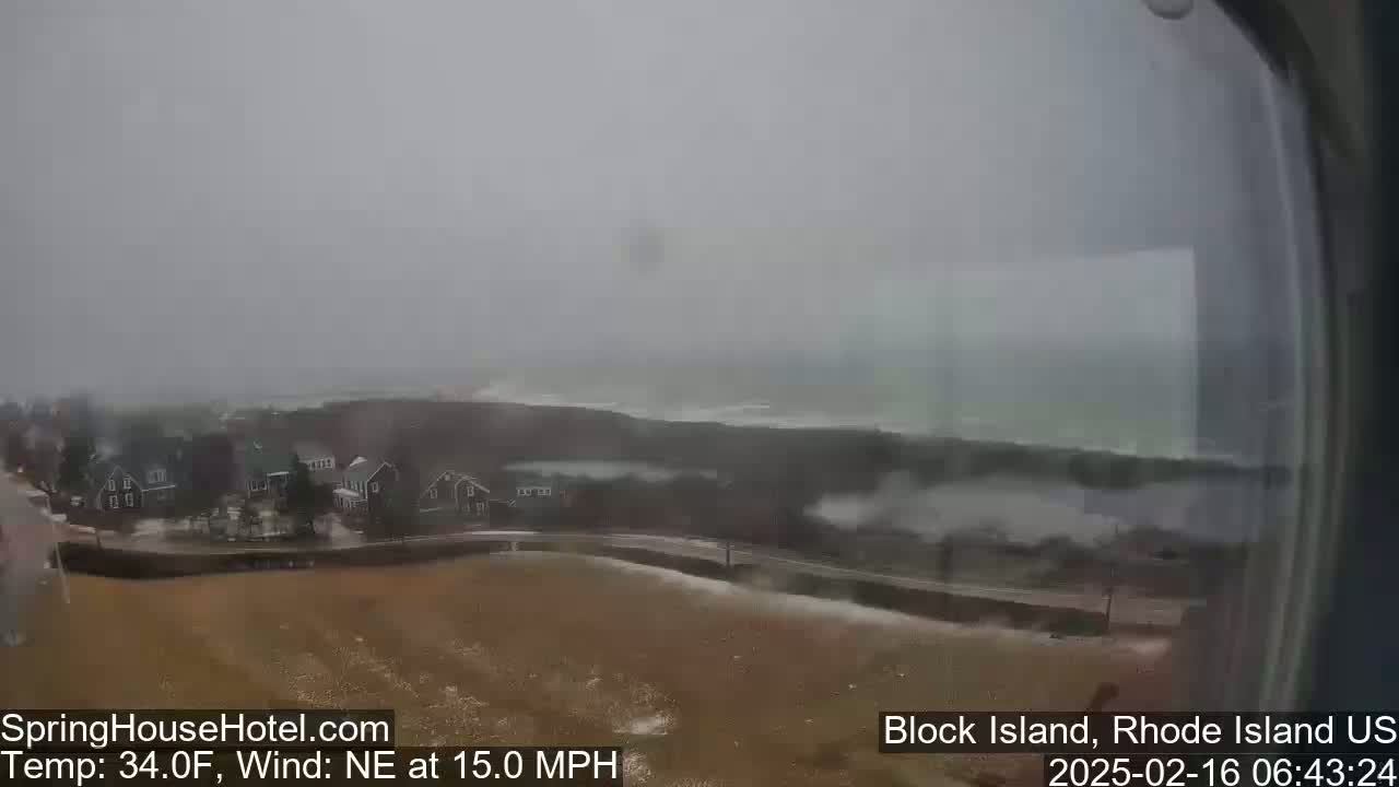 A coastal town is seen under stormy conditions with a northeast wind of 15 mph and a temperature of 34°F;  rough waves crash against the shore in the distance.