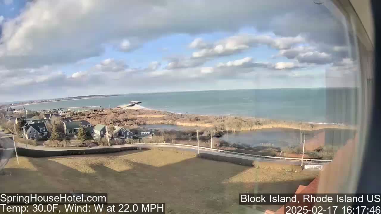 A coastal view shows a residential area overlooking a calm ocean under a partly cloudy sky with a 22 mph westerly wind.