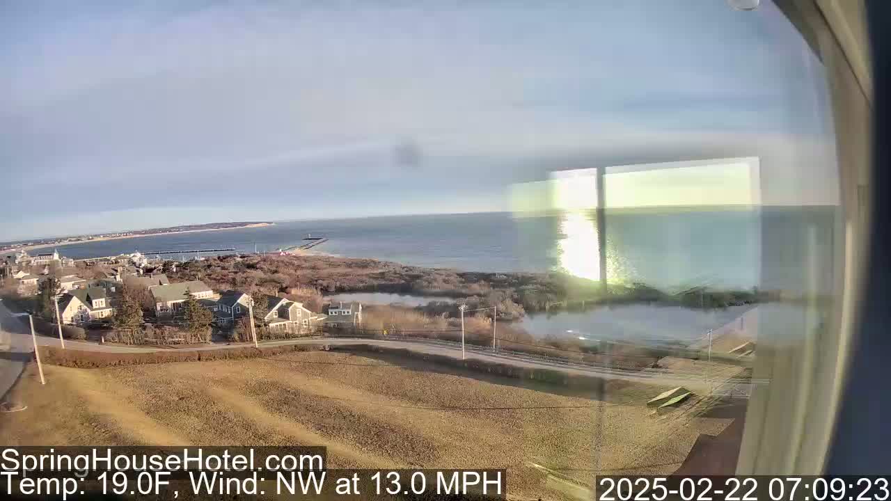 A coastal scene with calm waters and houses, seen through a window on a cold, clear morning with a northwest wind at 13 mph.