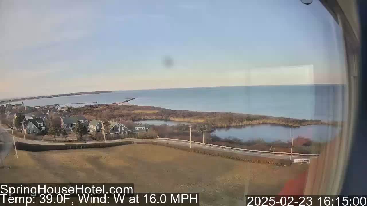 A seaside residential area with a calm ocean and a small pond under a clear sky, with a 16 mph west wind and a temperature of 39°F.