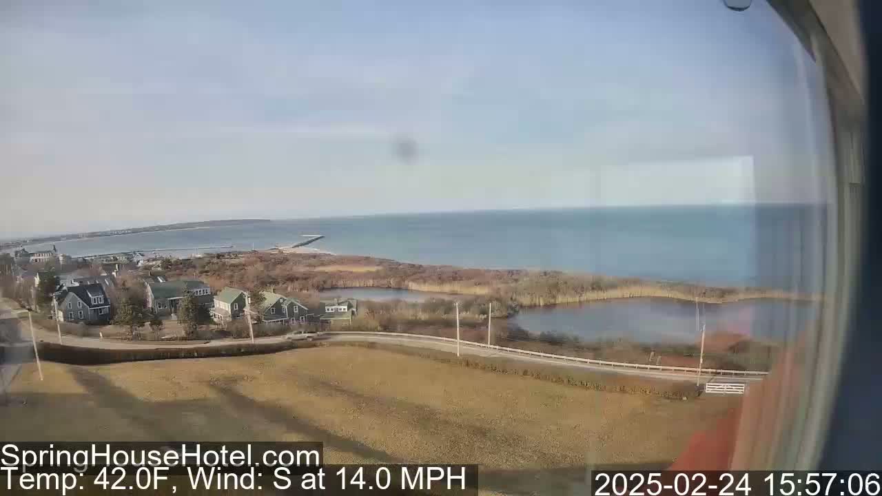 A coastal view on a partly sunny day shows a calm ocean, houses, marshland, and a road, with a south wind blowing at 14 mph and a temperature of 42°F.