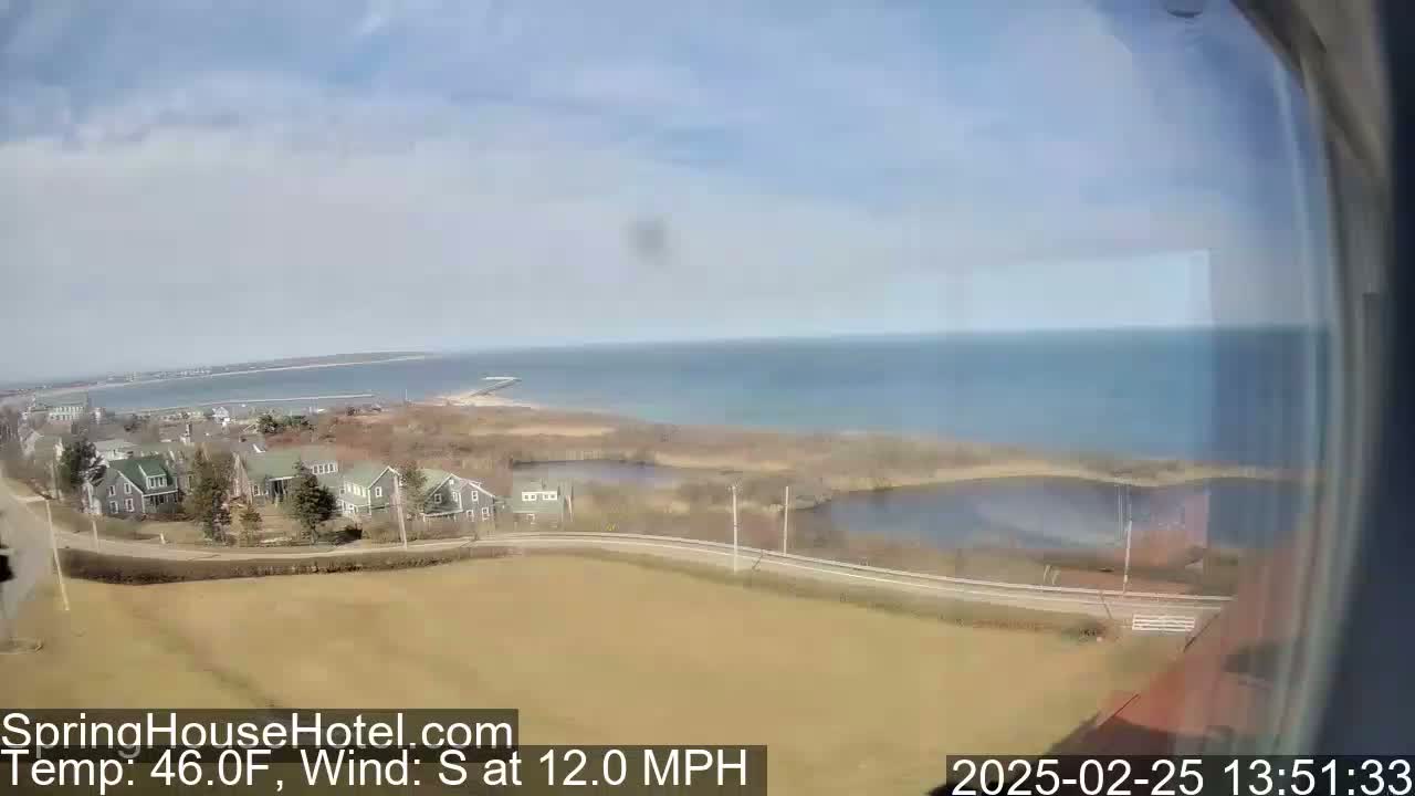A seaside view shows a calm ocean, a road winding through houses near a body of water, and a mostly sunny sky with a south wind of 12 mph and a temperature of 46°F.
