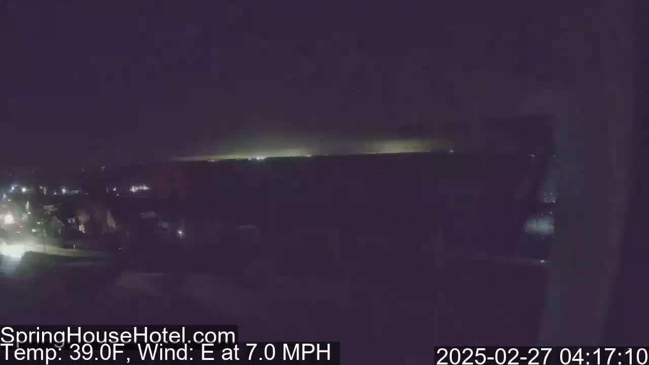 A nighttime, long shot of a city landscape with a faint, light horizon under an overcast sky, and an easterly wind of 7 mph at 39°F.