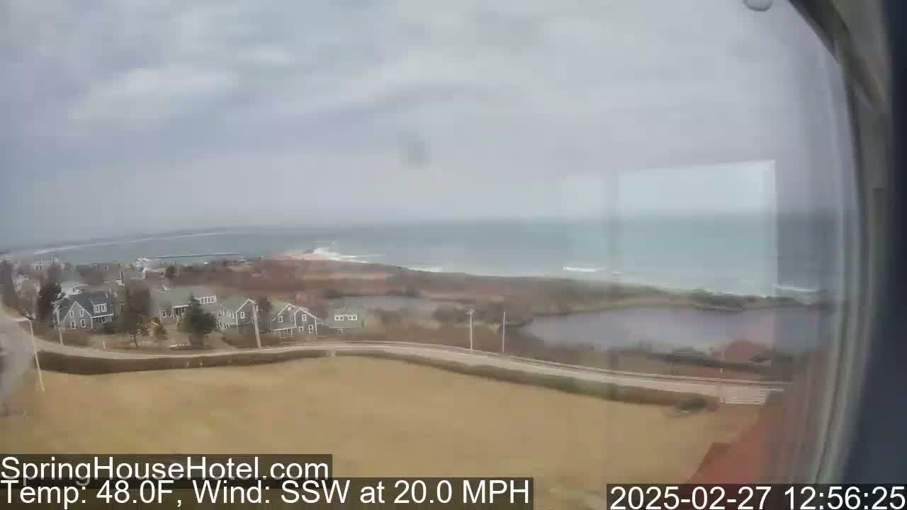 A coastal view shows a cluster of houses near the ocean under an overcast sky with a 20 mph southwest wind.