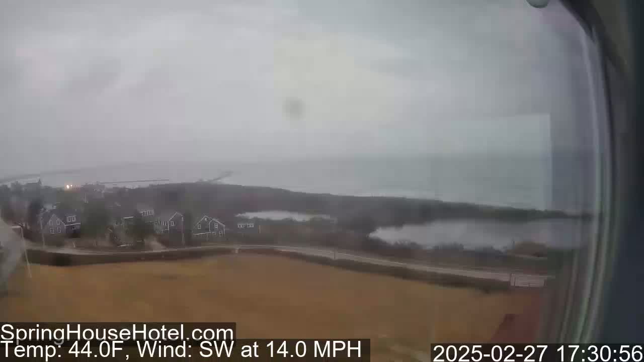 A hazy, overcast view shows a coastal area with houses and a body of water under a gray sky, with a southwest wind blowing at 14 miles per hour.