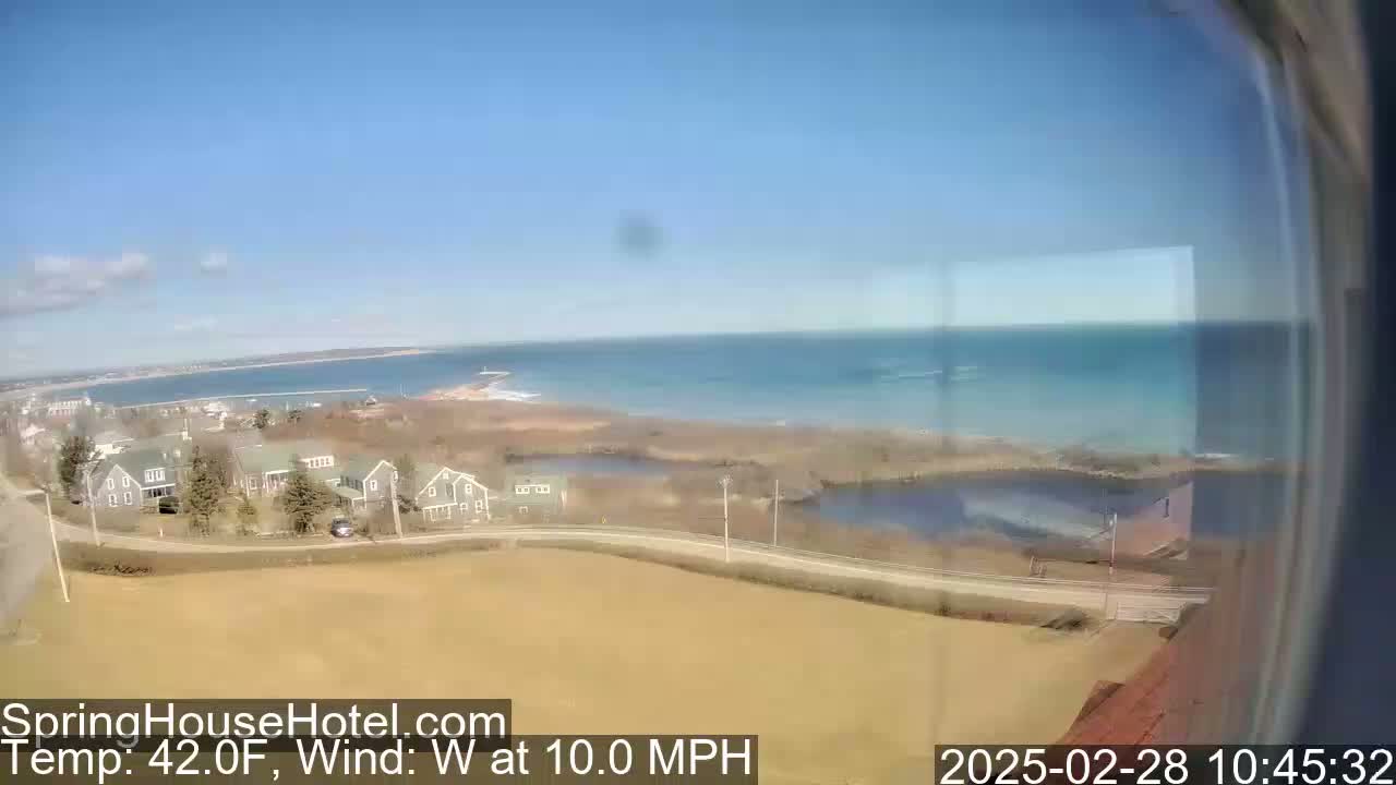 A coastal scene on a clear, breezy day shows a calm ocean, a shoreline with houses, and marshy areas, with a westerly wind of 10 mph and a temperature of 42°F.