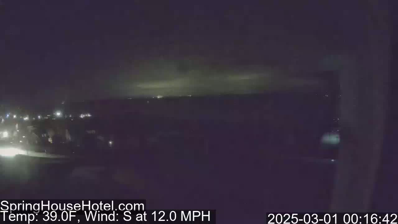 A nighttime view of city lights on the horizon under a dark sky with a 39°F temperature and a 12 mph south wind.