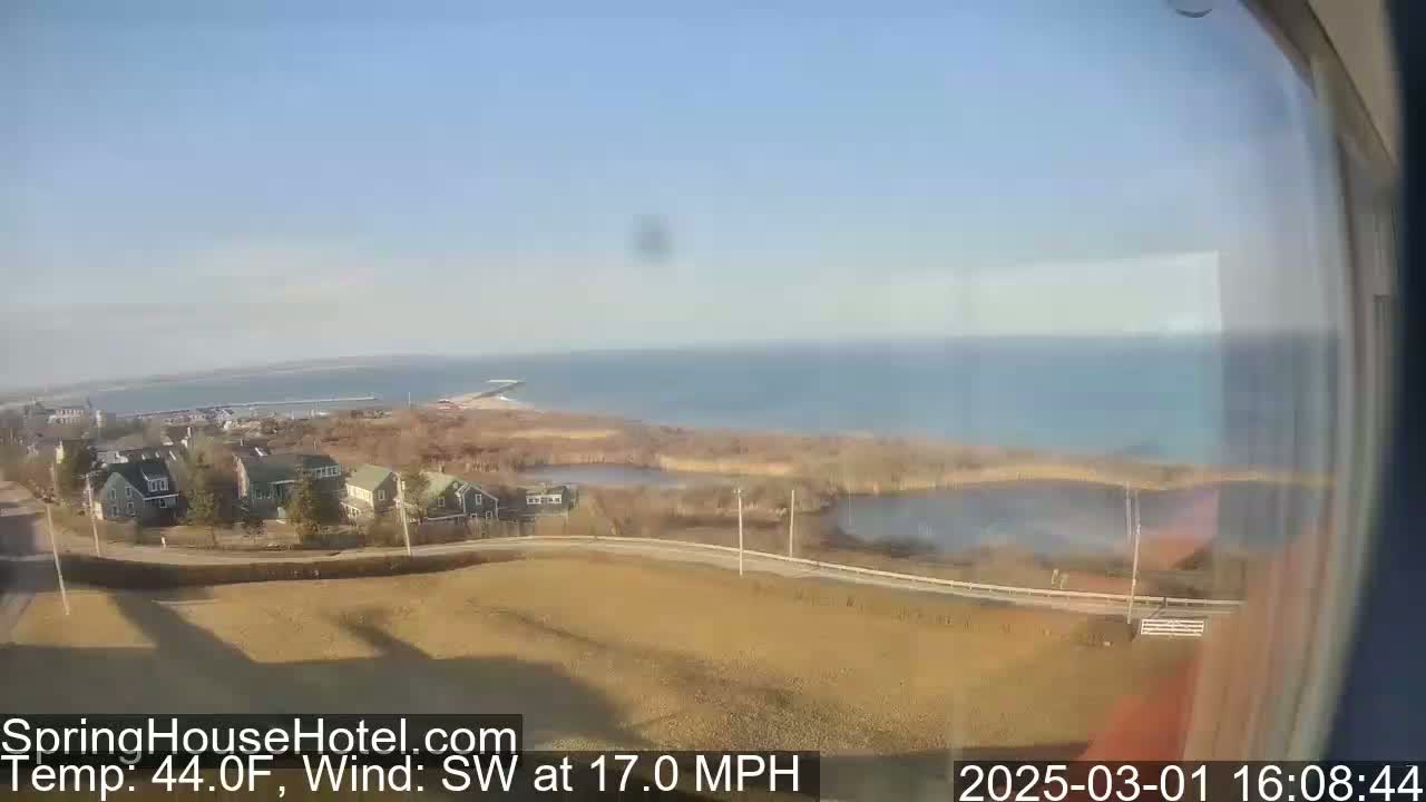 A view from a window shows a coastal town with houses and a body of water under a clear sky, with a southwest wind at 17 miles per hour and a temperature of 44 degrees Fahrenheit.