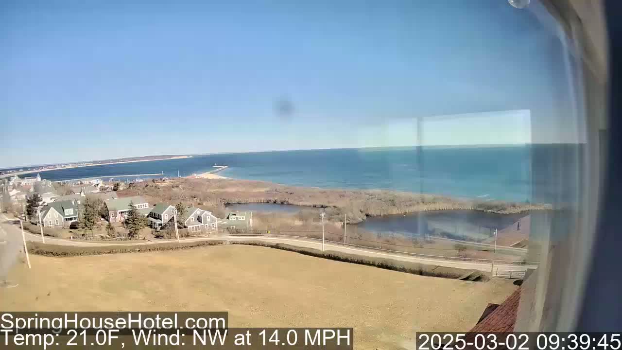 A high-angle view shows a coastal town on a clear, sunny day with a northwest wind at 14 miles per hour and a temperature of 21 degrees Fahrenheit.