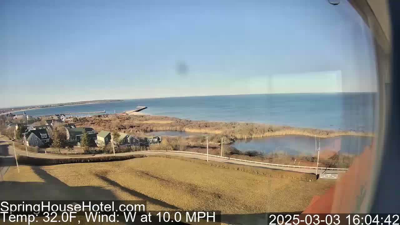 A coastal scene on a sunny day with a 32°F temperature and a 10 mph west wind shows a calm body of water, a small town with houses, and a marshy area.