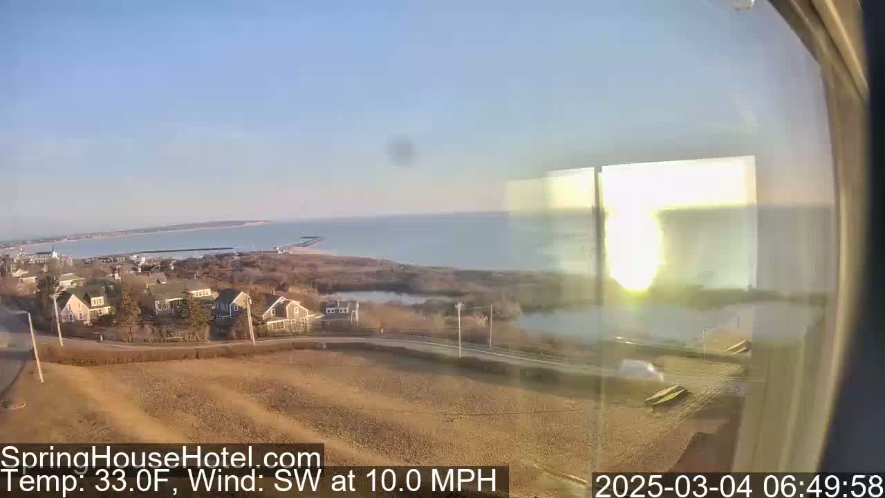 A coastal view on a clear, sunny morning shows a small town with houses near a body of water, with a 10 mph southwest wind.