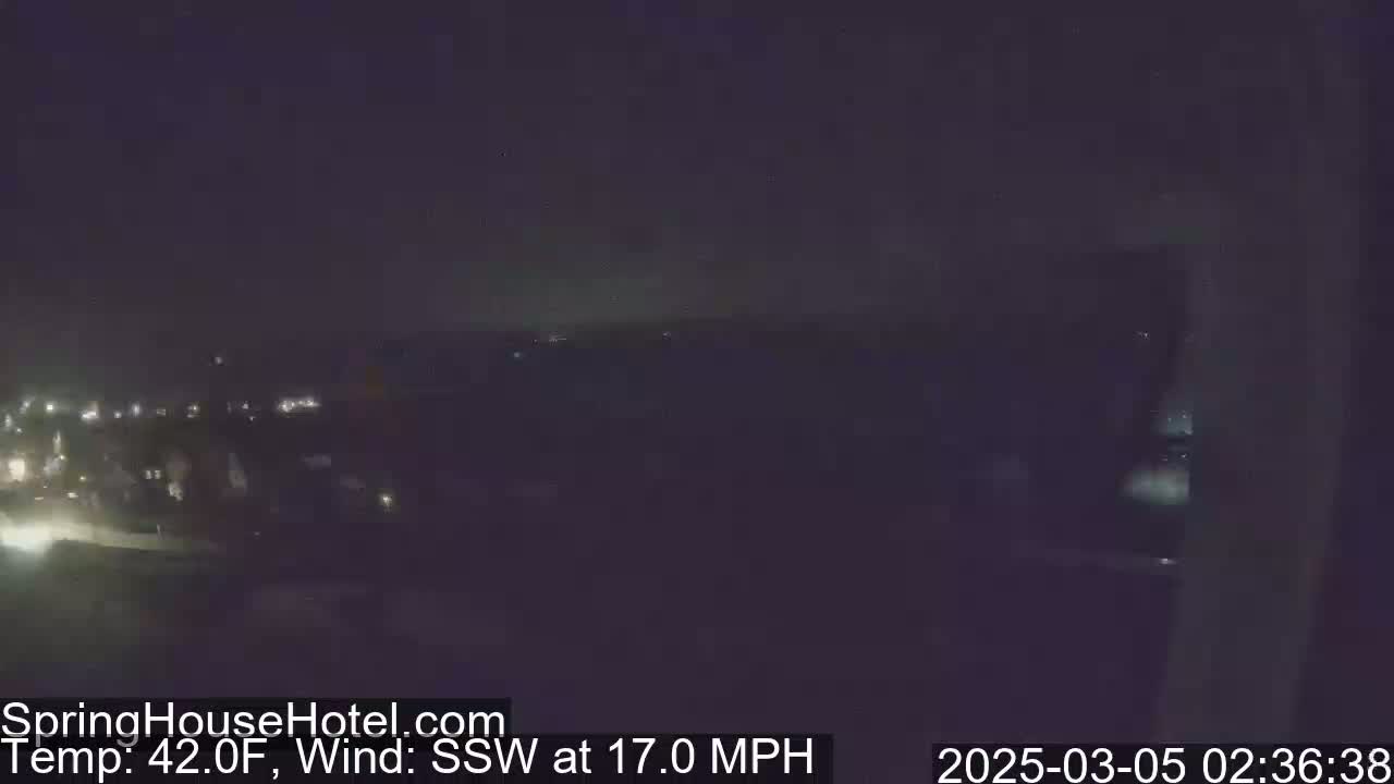 A nighttime, long-distance view of a dimly lit town under a dark sky with a south-southwesterly wind blowing at 17 miles per hour and a temperature of 42 degrees Fahrenheit.