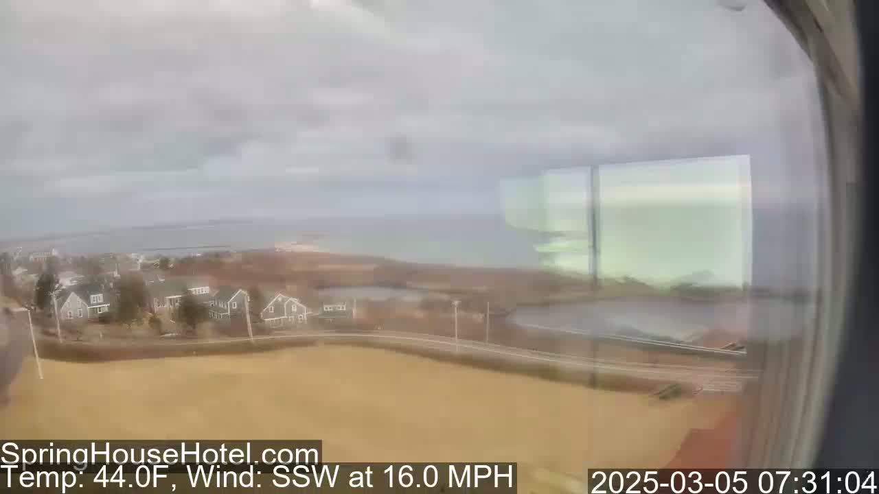 A coastal view on an overcast day shows a residential area with a body of water in the background and a 16 mph wind from the south-southwest.