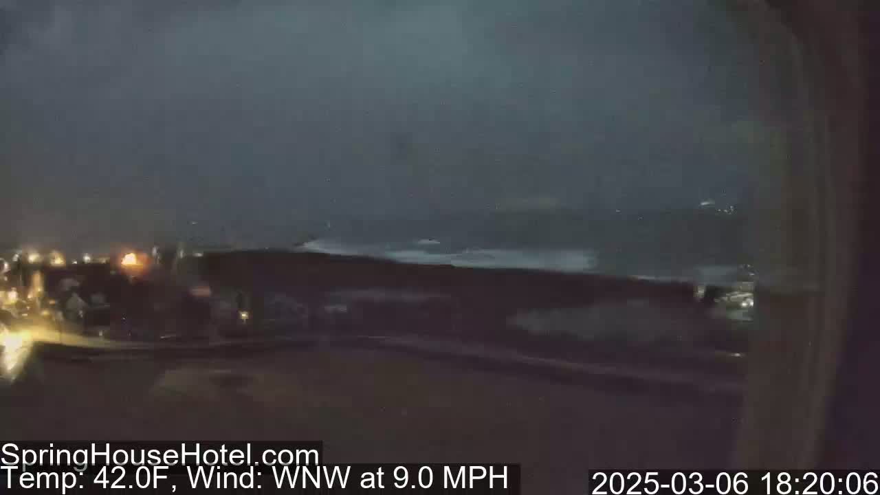 A nighttime outdoor scene shows a dark, stormy sky with a WNW wind at 9.0 mph and a temperature of 42°F, overlooking dimly lit buildings and vehicles.