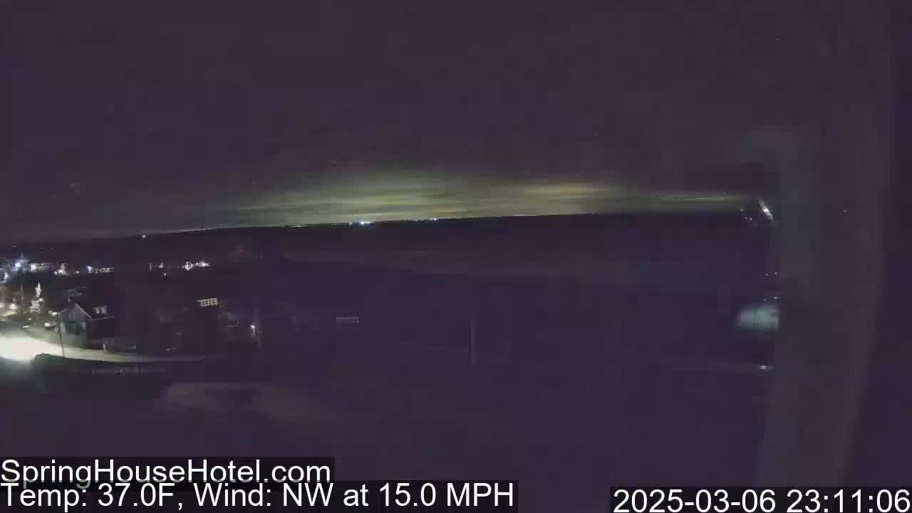 A nighttime view of a town, illuminated by faint lights, under a mostly clear sky with a northwest wind blowing at 15 mph.
