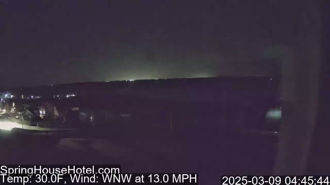 A nighttime, long-range view of a suburban area under a dark sky with a 30°F temperature and a 13 mph wind from the west-northwest.