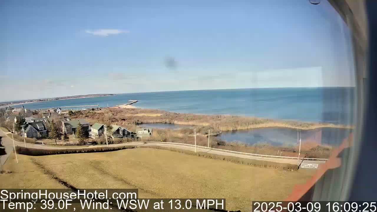 A coastal scene on a clear, sunny day with a 13 mph wind shows a calm ocean, houses, marshland, and a road curving towards the water.