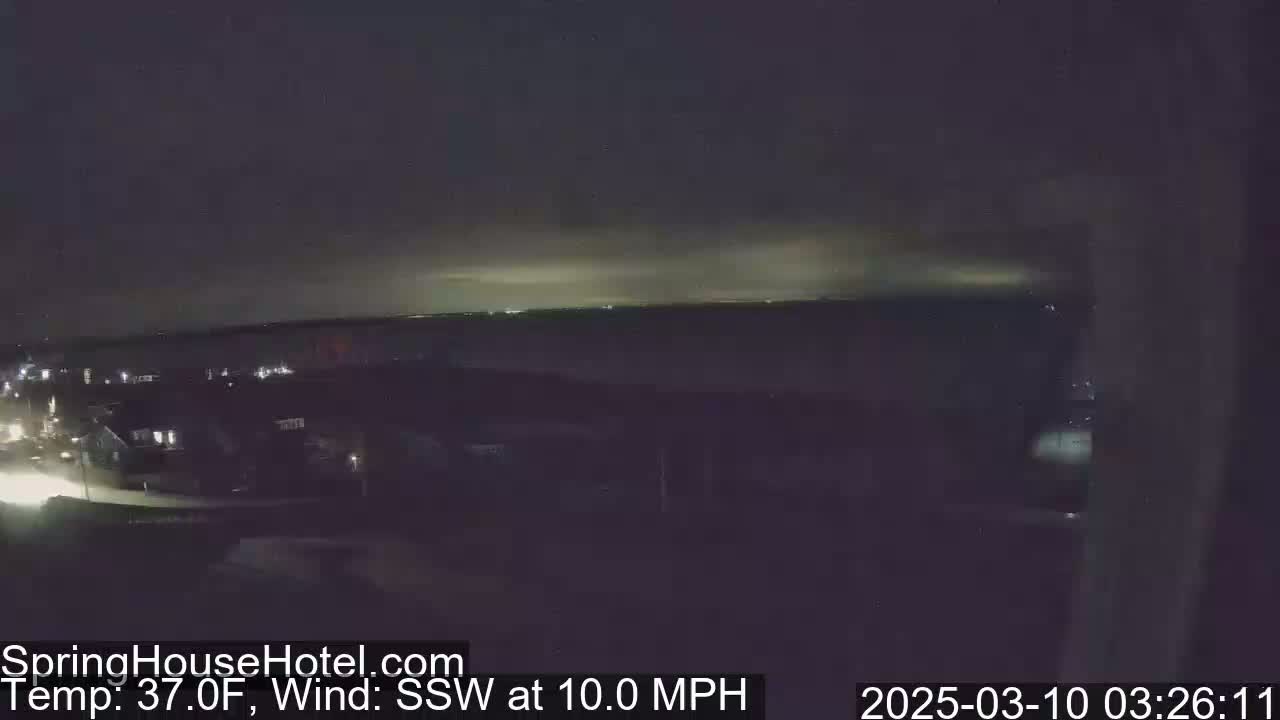 A nighttime view of a town's lights in the distance under a dark, cloudy sky, with a 37°F temperature and a 10 mph south-southwest wind.