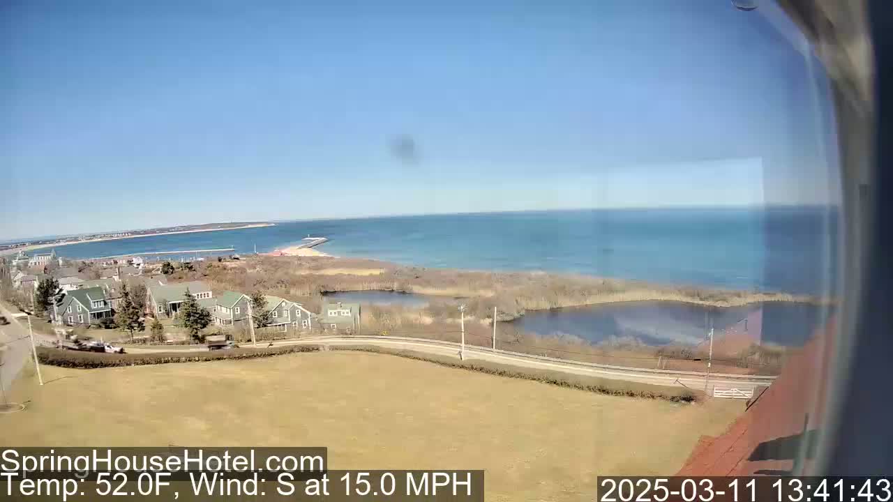 A coastal scene on a sunny day with a 15 mph south wind shows a calm ocean, houses, and marshland near a road.