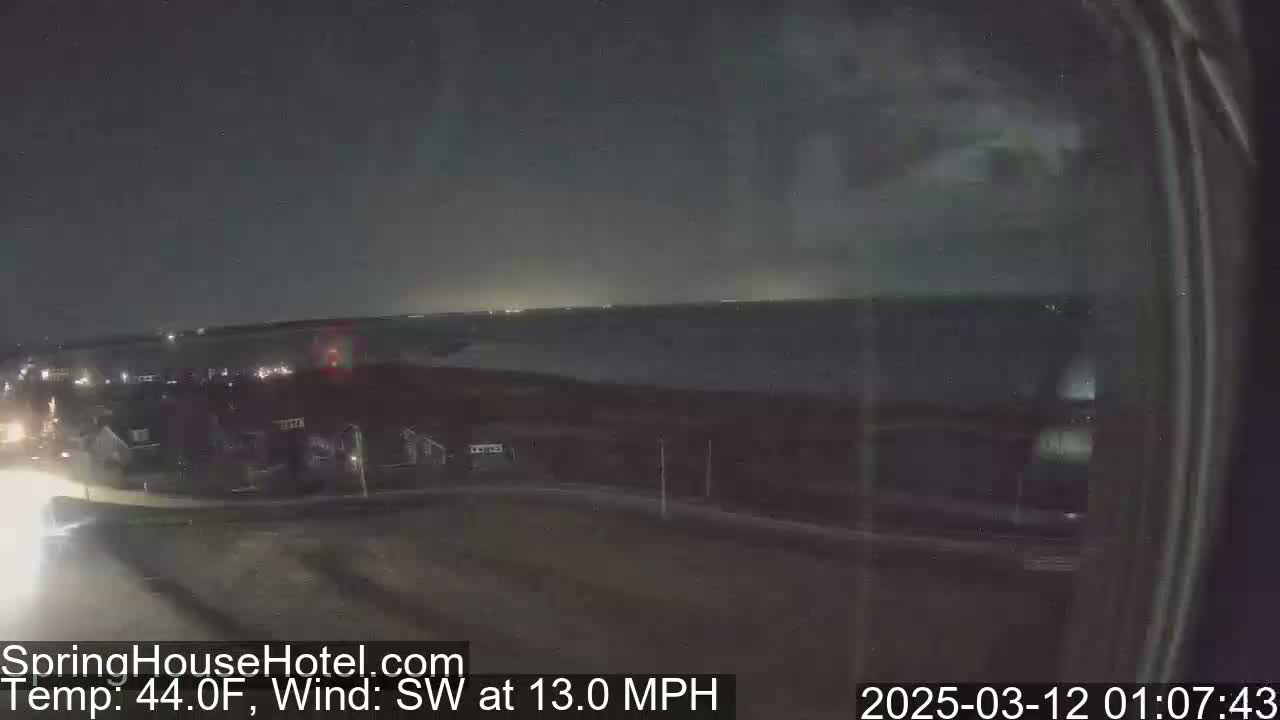 A nighttime view of a residential area with a road, under a dark sky with a southwest wind of 13 mph and a temperature of 44°F.
