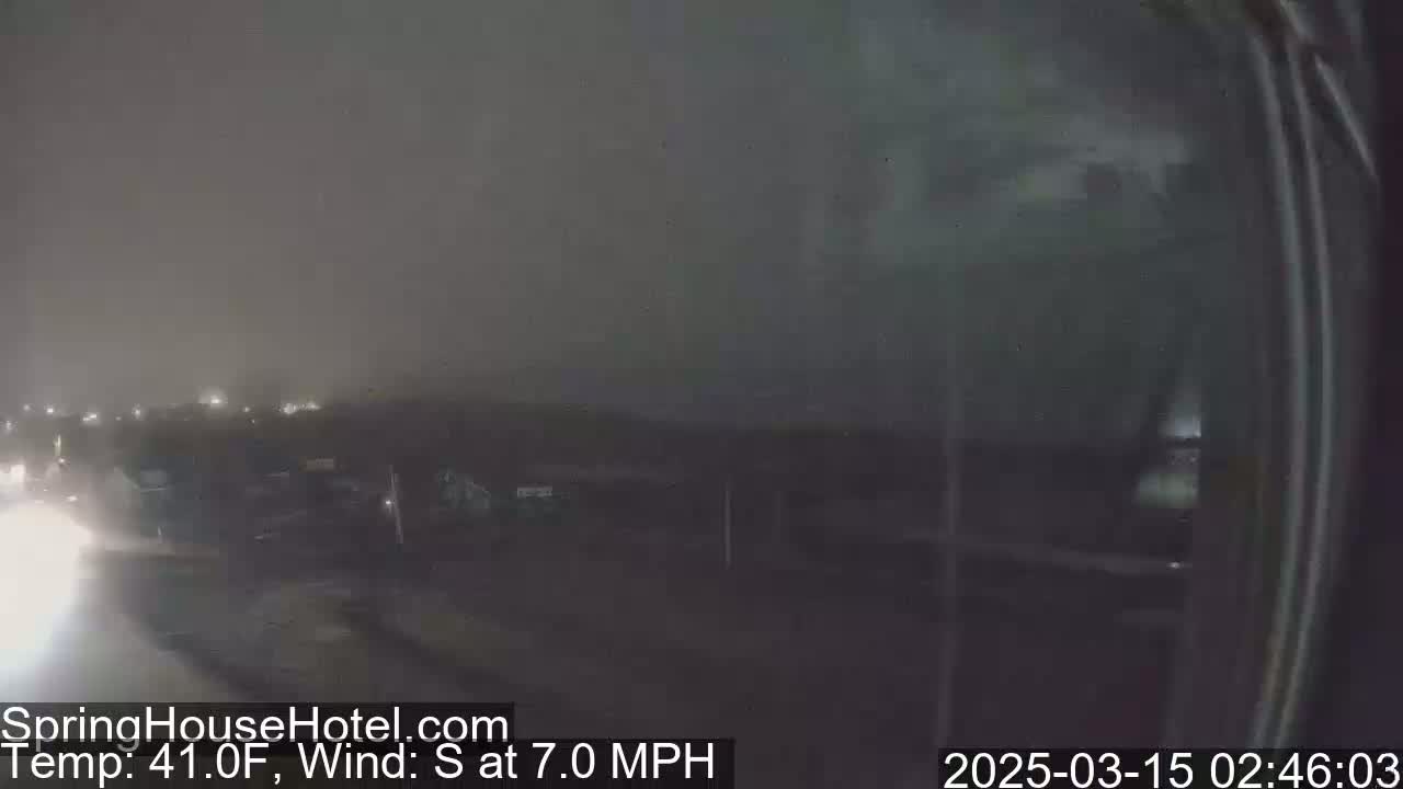 A nighttime, hazy scene of a roadway with buildings and vehicles in the distance under a 41°F temperature and a 7 mph south wind.