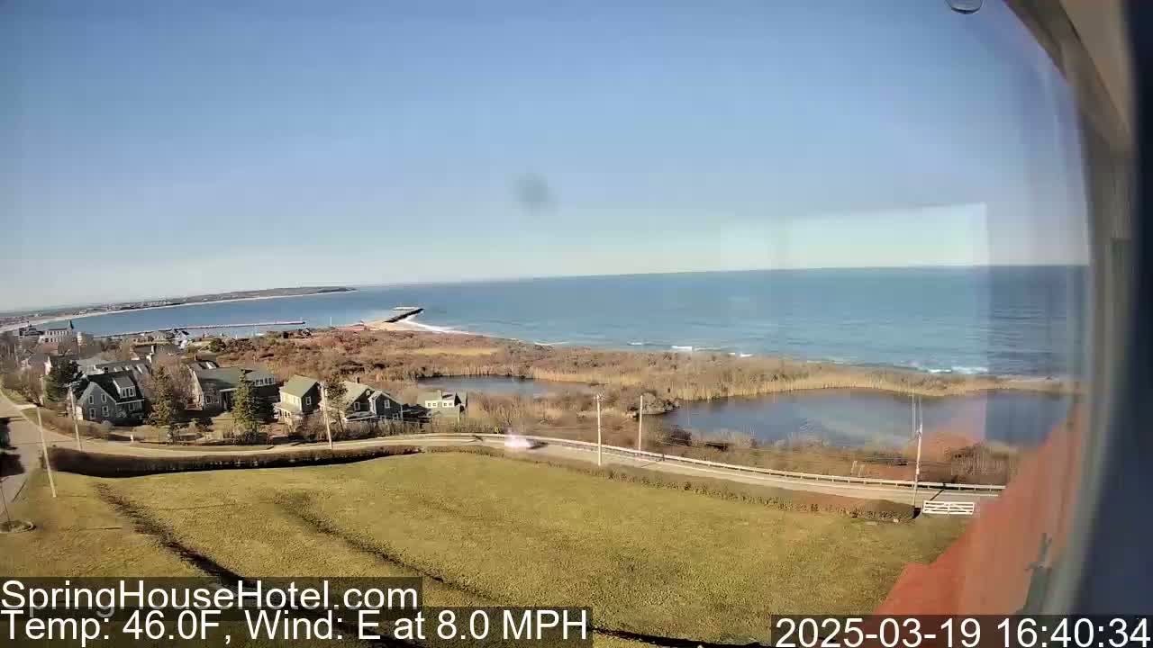 A coastal scene on a sunny day with an 8 mph east wind shows a calm ocean, a small town nestled near the shore, and a marshy area separating the town from the water.