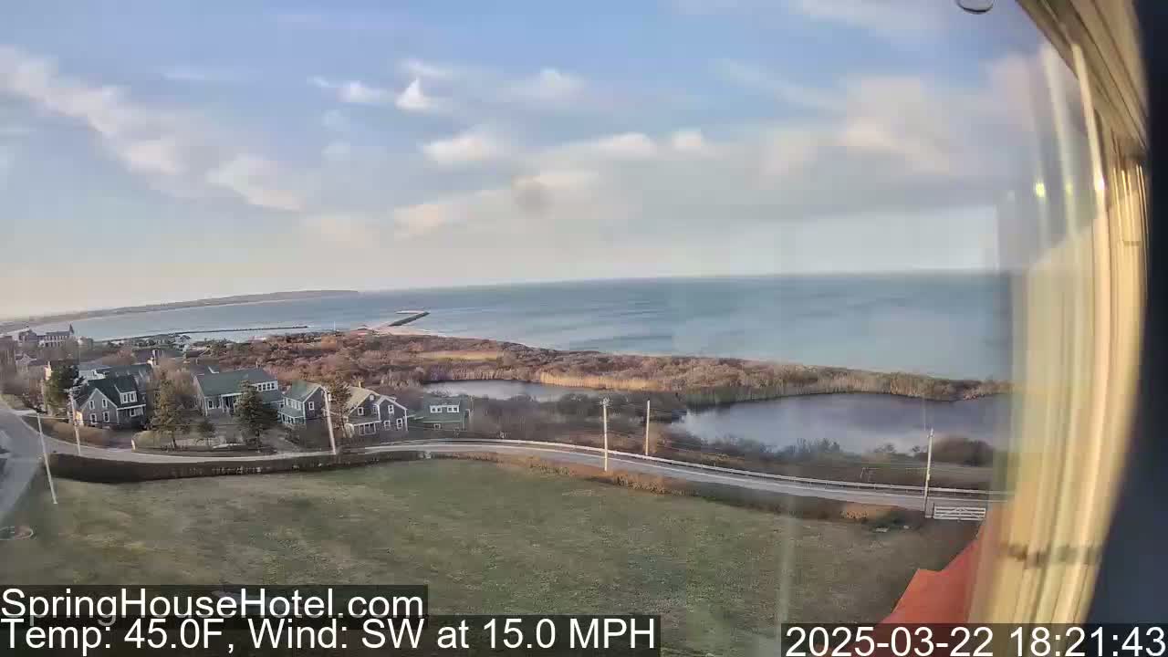 A coastal view shows a calm ocean under a partly cloudy sky, with houses and a road visible in the foreground.