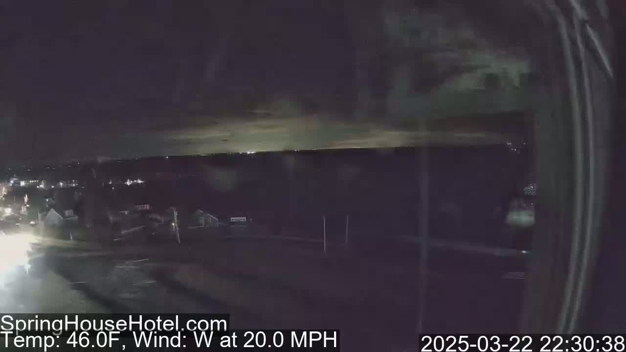 A nighttime, elevated view of a town under a partly cloudy sky with a 20 mph westerly wind and a temperature of 46 degrees Fahrenheit.