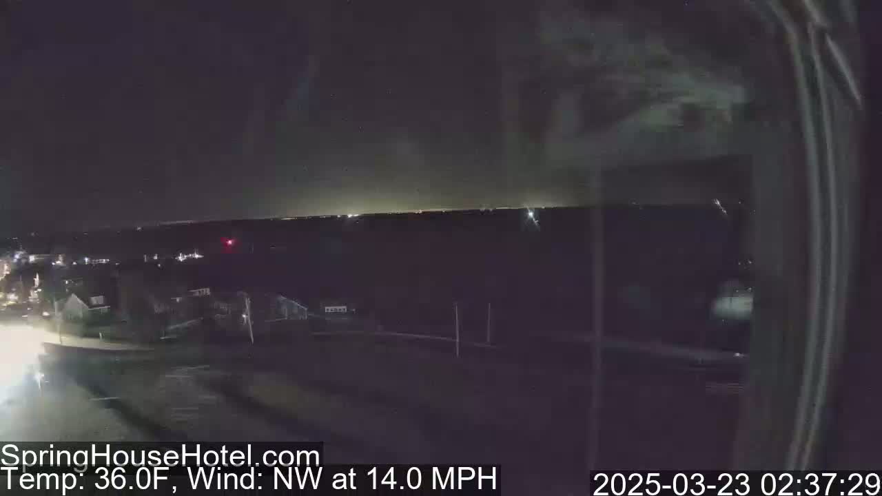 A nighttime, long shot of a road and houses, with a northwest wind at 14 mph and a temperature of 36 degrees Fahrenheit.