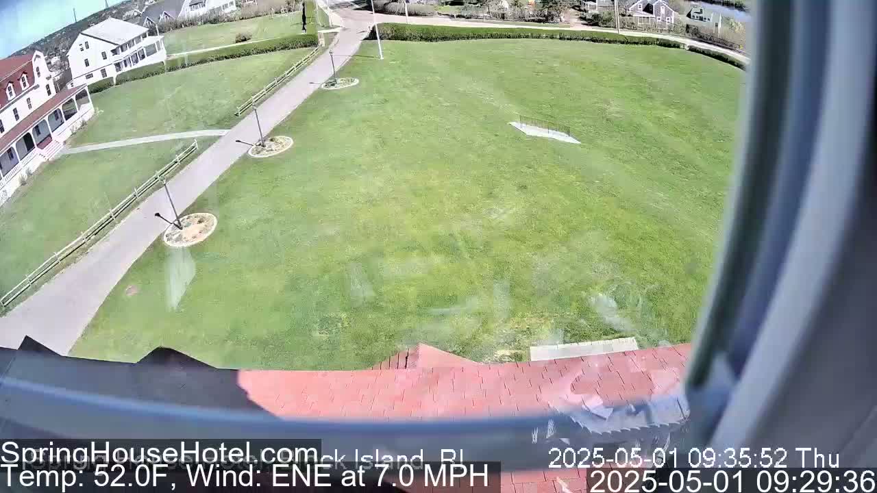 A view from a window shows a large grassy area with paved walkways, buildings in the background, and a slight breeze.