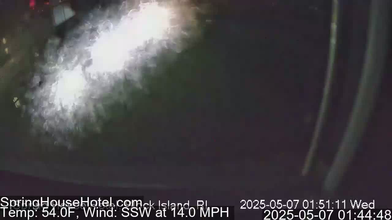 A blurry nighttime image shows bright headlights reflecting off a wet surface in a strong south-southwesterly wind at 54°F.