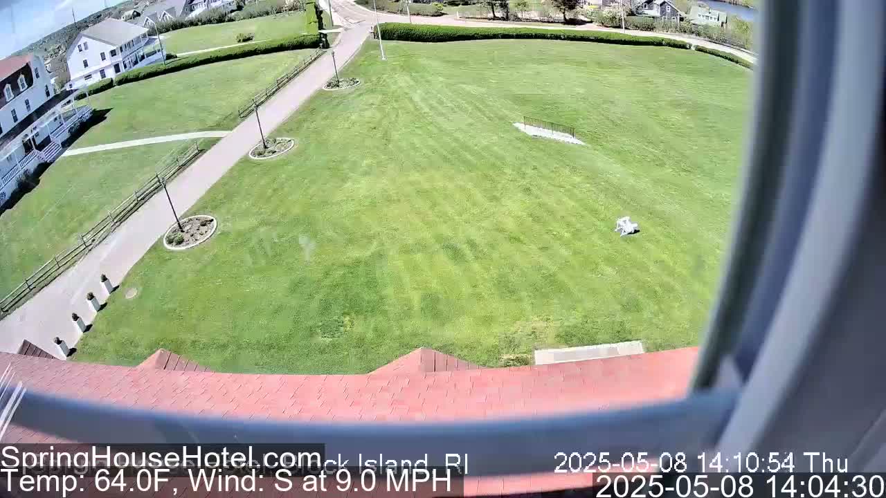 A large grassy area with paths and a building is seen from an elevated viewpoint on a sunny day with a south wind.