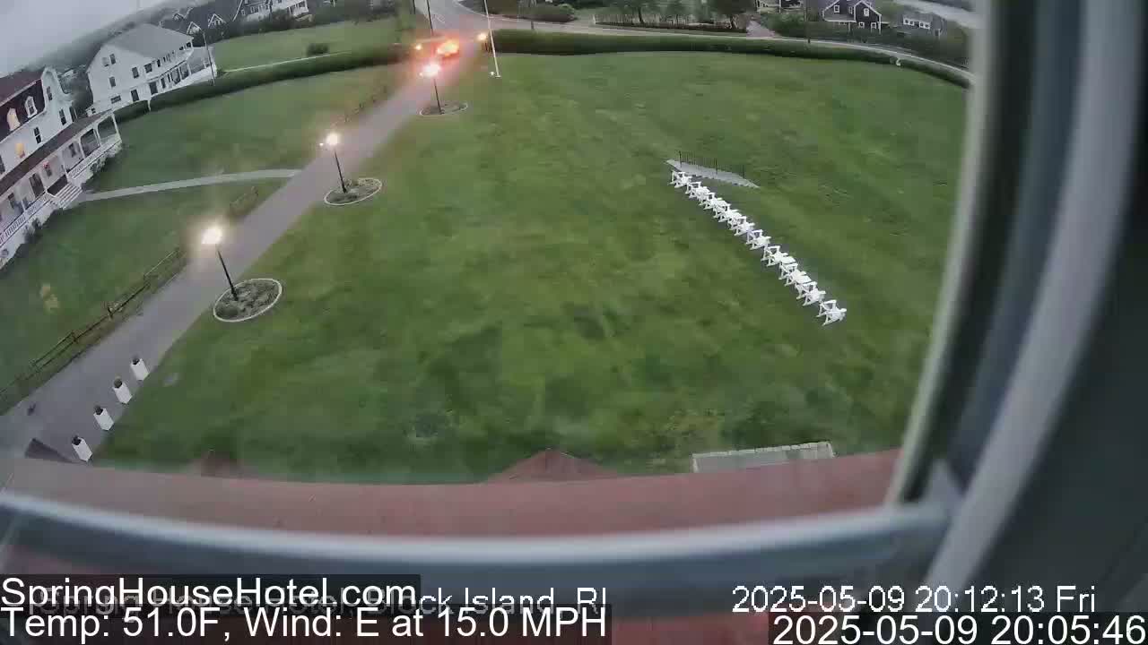 A grassy lawn with a row of white chairs is viewed from above on a partly cloudy evening, with an easterly wind at 15 mph and a temperature of 51°F.