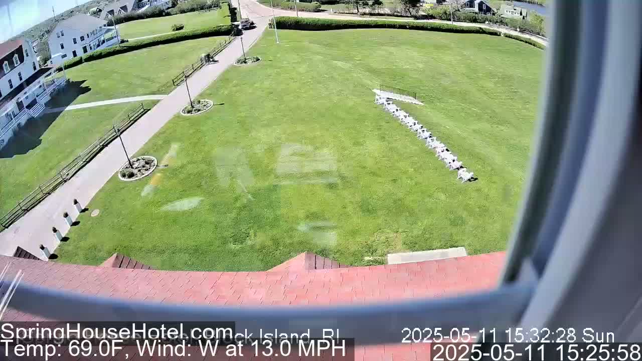 A sunny day with a west wind of 13 mph shows a view of a lawn with chairs lined up, a building, and a paved walkway.