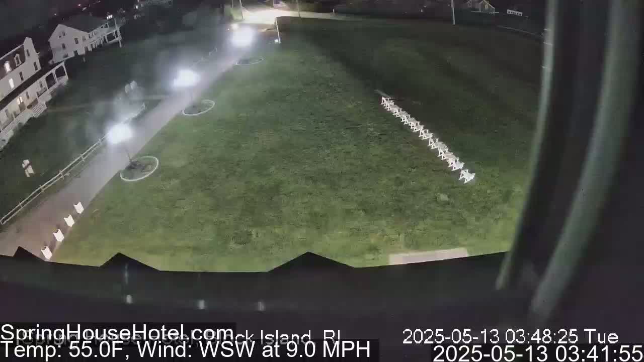 A nighttime, slightly misty view of a grassy area with a line of chairs and a building in the background, under a WSW wind of 9.0 MPH and 55°F temperature.