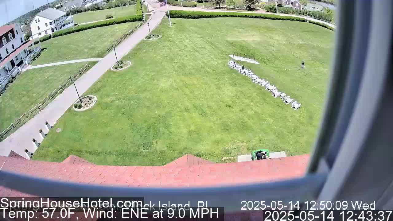 A high-angle view shows a large grassy area with a row of chairs, a building, and walkways, all under sunny conditions with a wind of 9.0 mph from the east-northeast.