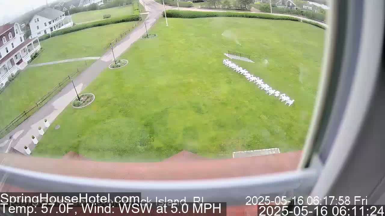 A grassy lawn with a row of white chairs is seen from an elevated viewpoint on a partly cloudy day with a wind of 5.0 mph from the west-southwest, and a temperature of 57 degrees Fahrenheit.