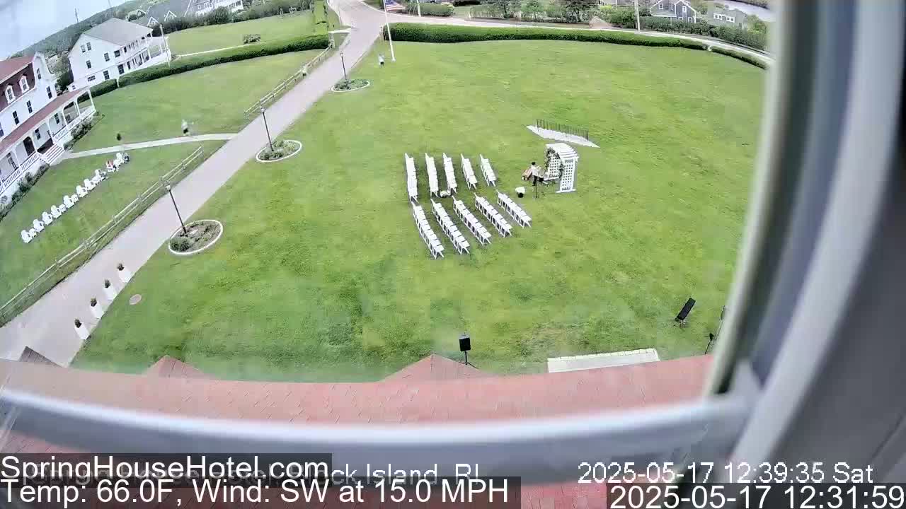 An outdoor wedding setup with white chairs arranged in rows on a grassy lawn near a building, under a partly cloudy sky with a southwest wind of 15 mph and a temperature of 66°F.