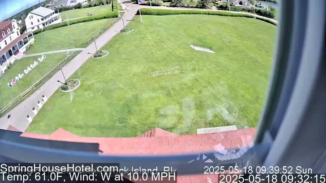 A large grassy area is viewed from an elevated position on a sunny day with a west wind of 10 mph, showing a building and walkways.