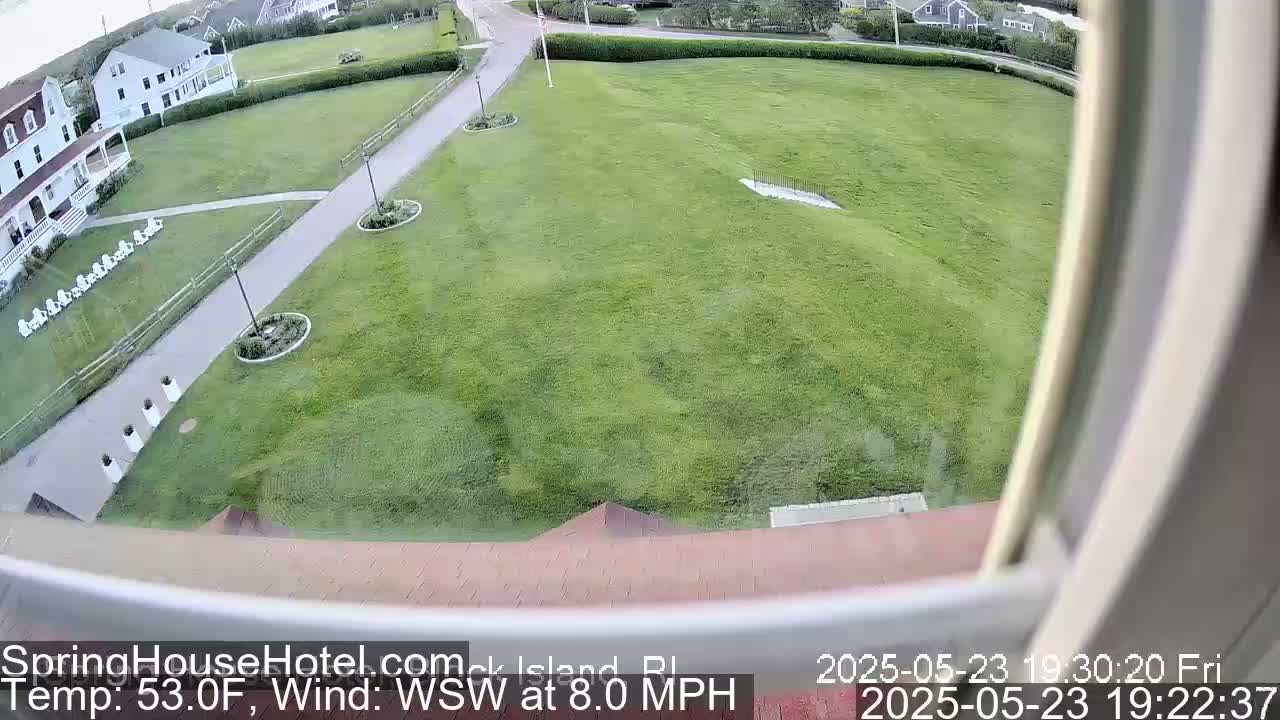 A high-angle view from a window shows a grassy lawn, a paved walkway, and several buildings in the background, with a wind of 8.0 mph from the west-southwest and a temperature of 53.0°F.