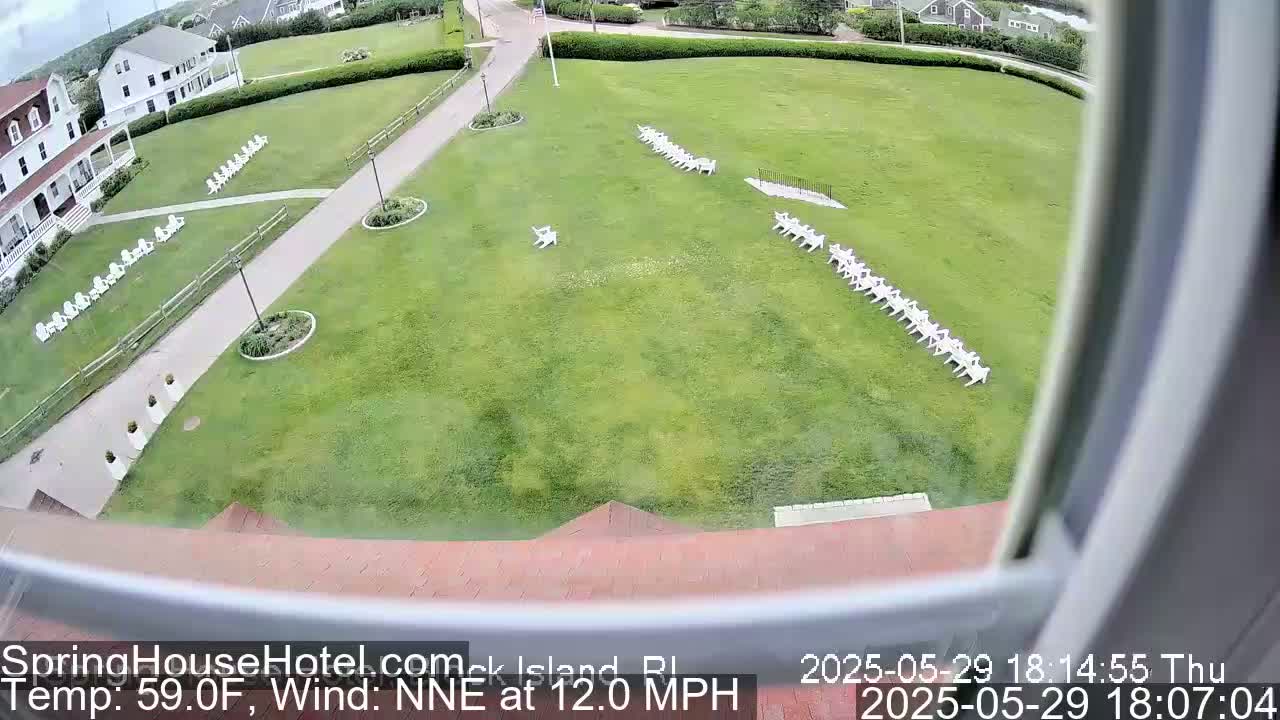 A large grassy area with rows of white chairs, seen from a window, on a partly cloudy day with a north-northeast wind at 12 mph.