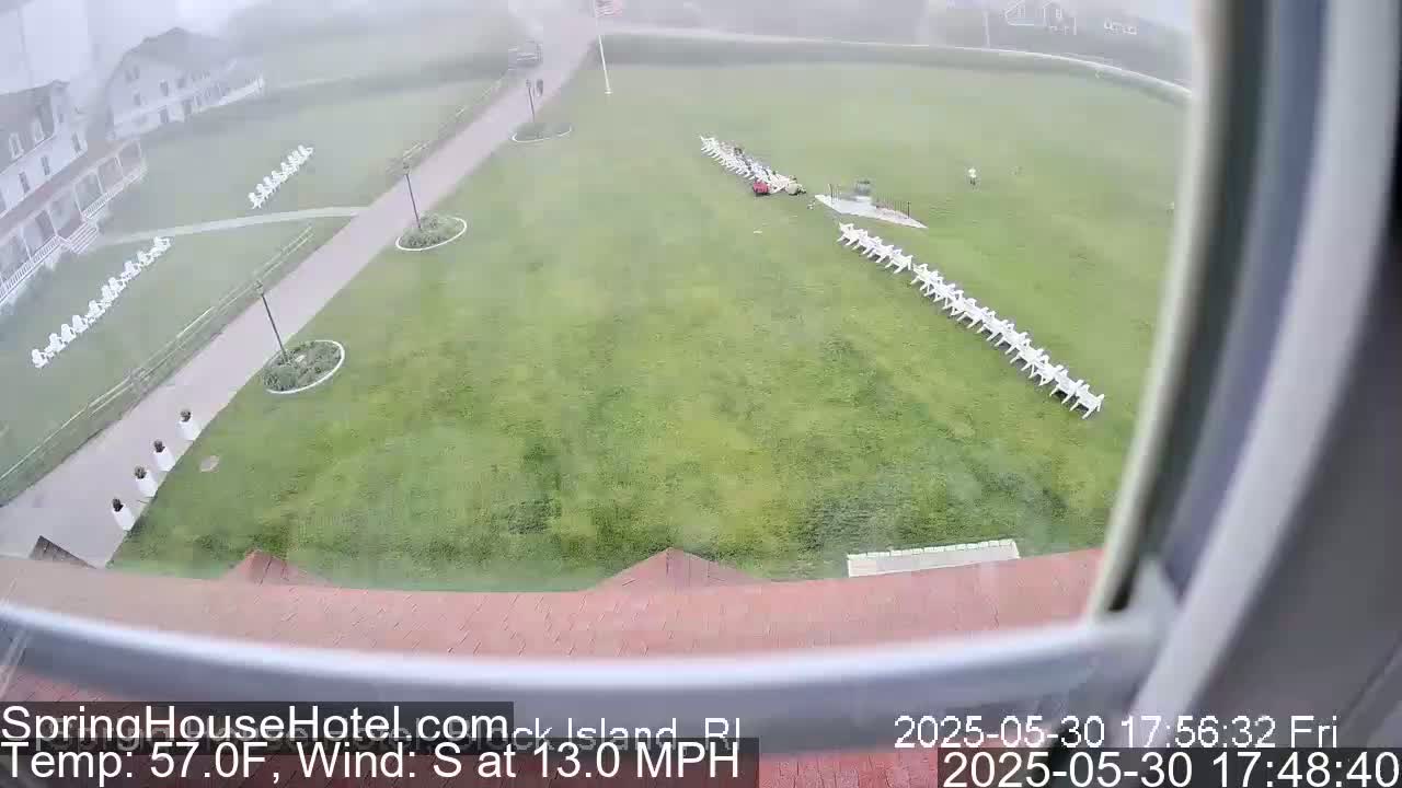 A foggy view from a window shows a large grassy area with rows of white chairs, a building, and a walkway.