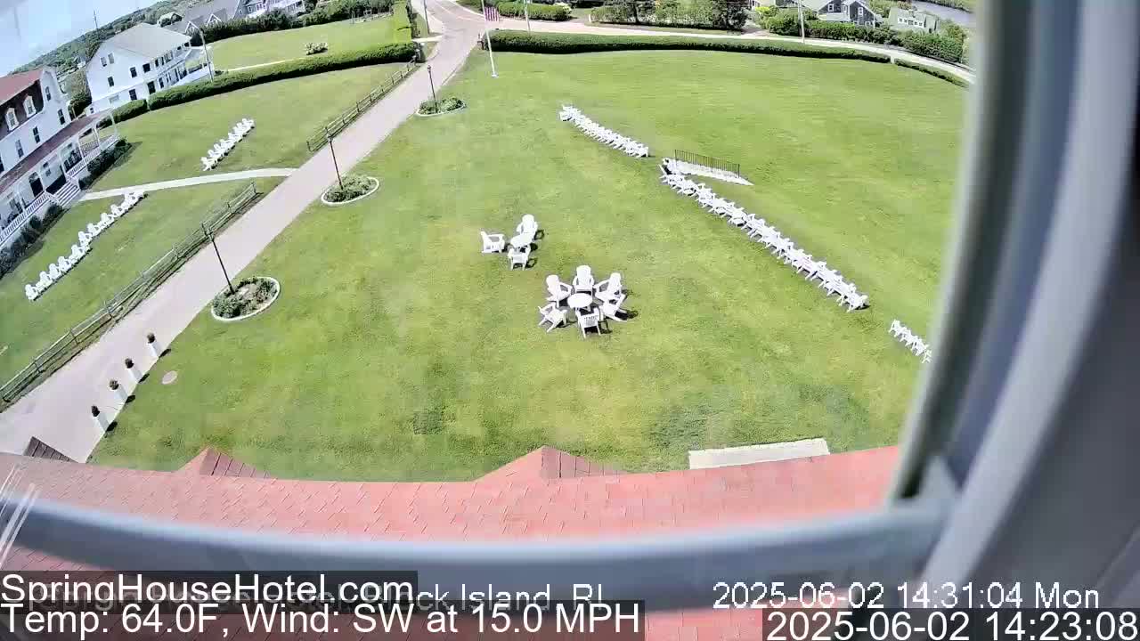 A large grassy area with numerous white chairs arranged in rows and small groups, viewed from above on a sunny day with a southwest wind at 15 mph.