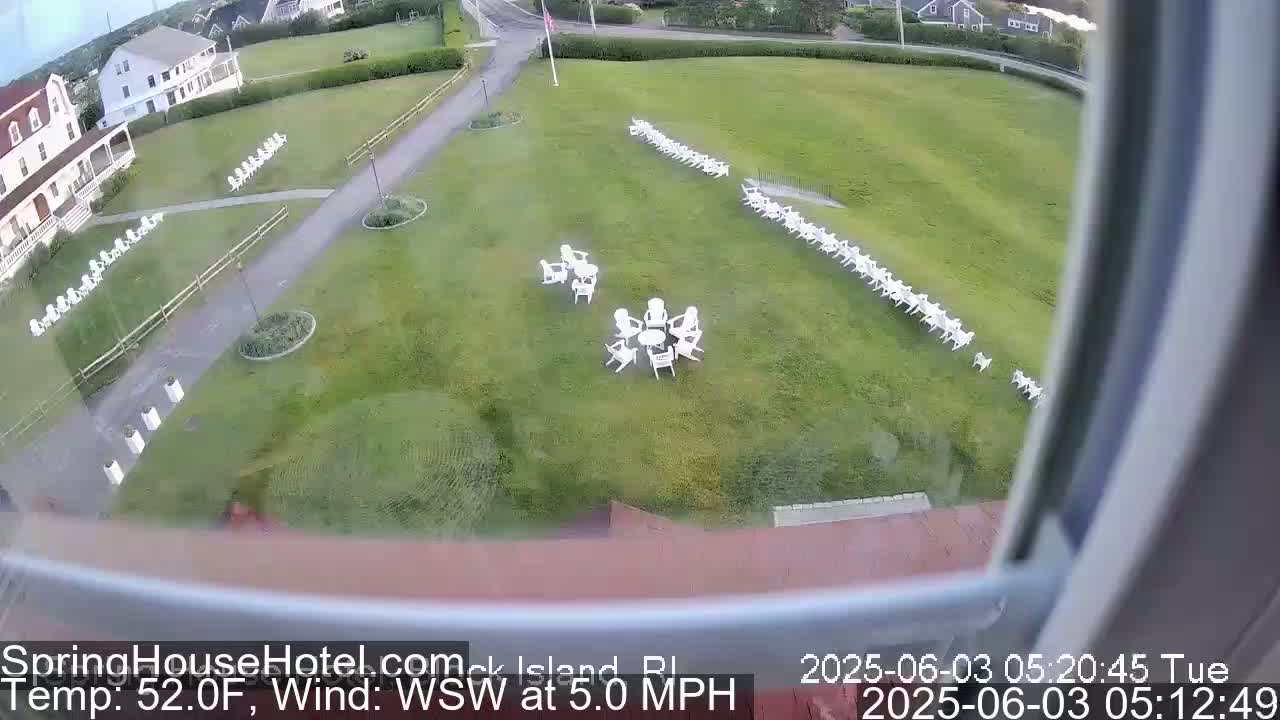 A grassy area with numerous white chairs arranged in rows and small groups, viewed from a window on a partly cloudy day with a 5 mph wind.