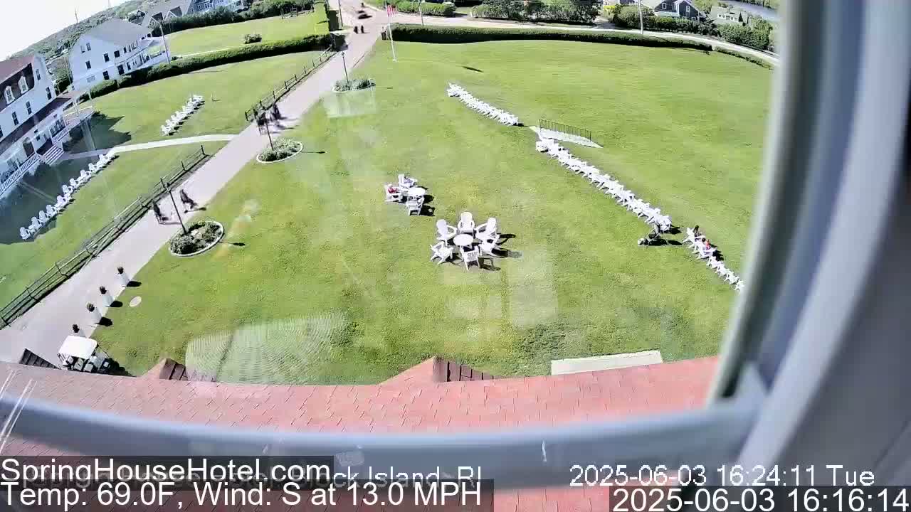 A large grassy area with numerous white chairs arranged in rows and small groups, viewed from a high angle on a sunny day with a south wind at 13 mph.